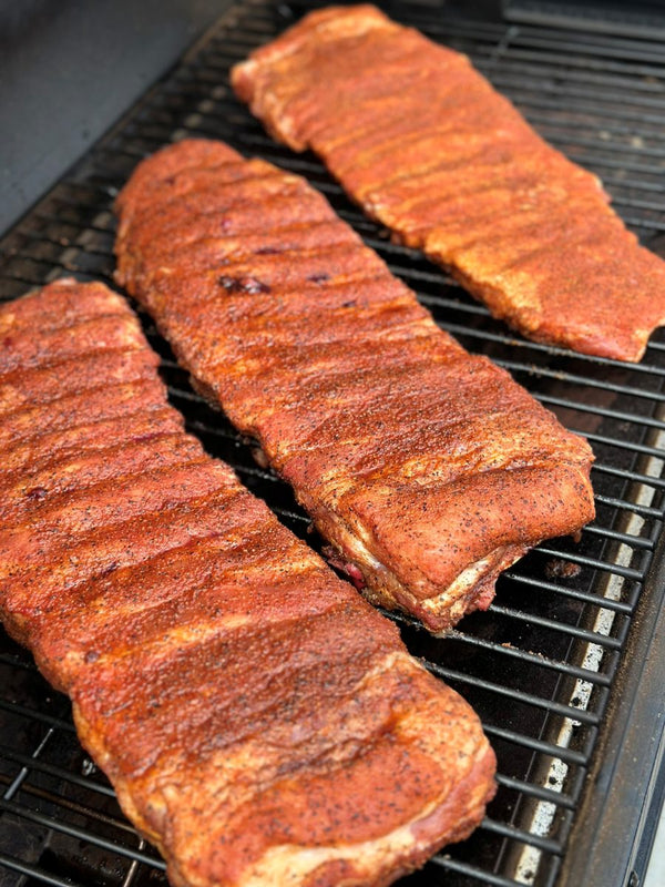 Racks of pork ribs with an even coat of rub on a smoker