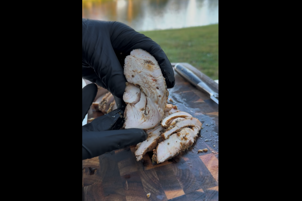 Sliced smoked turkey breast on a wooden carving board showing juicy interior and bronzed skin